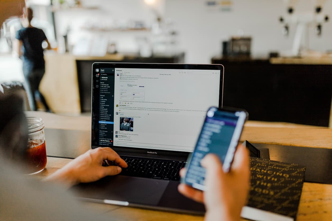 A marketer working across a laptop and a phone at a café table