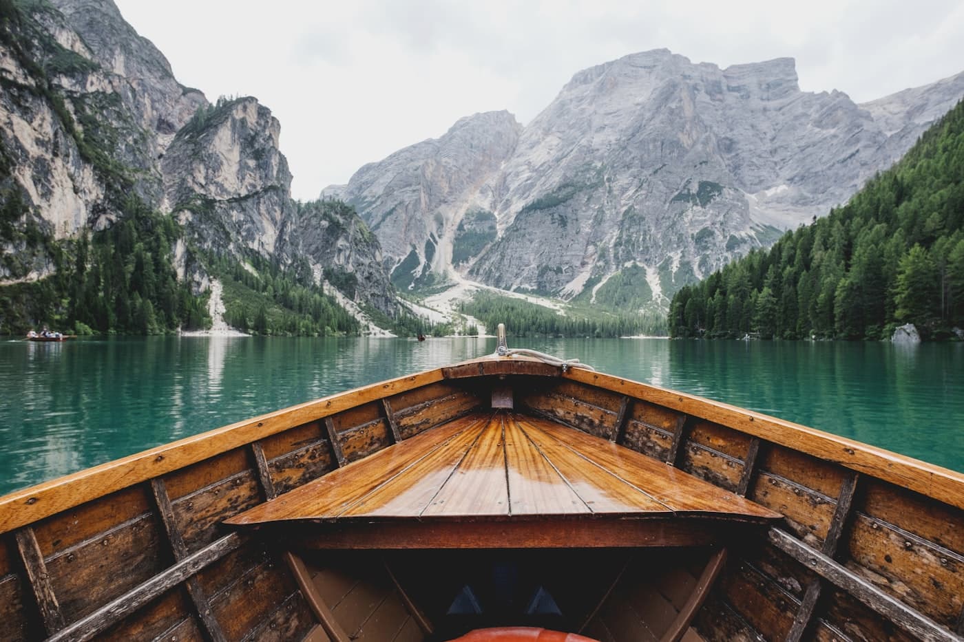 The bow of a wooden boat on a clear lake between mountains
