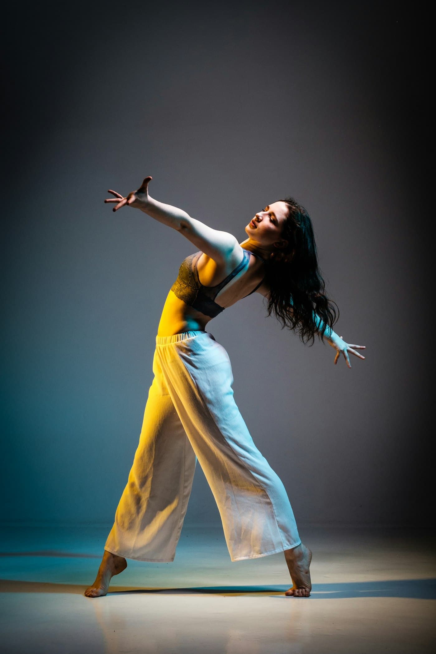 A dancer mid-move in yellow trousers against a dark wall