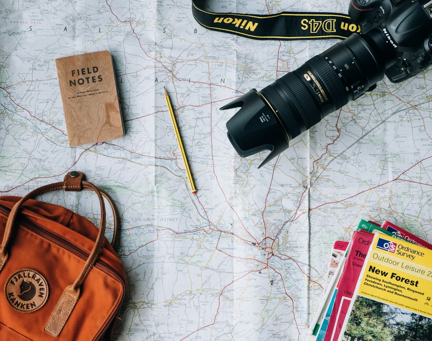 A camera, notebook and guidebooks laid out over a road map