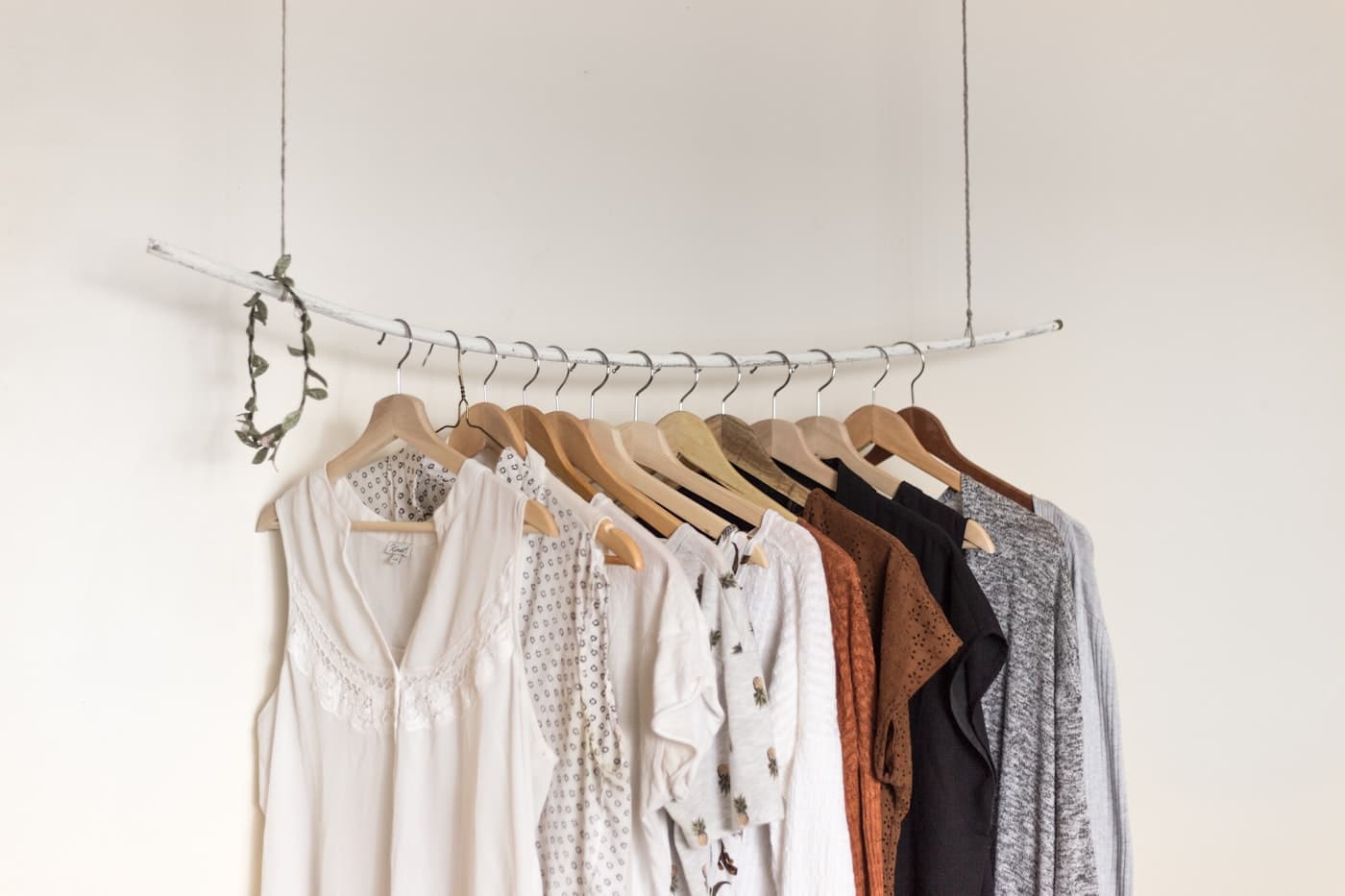 A tidy rail of clothes on wooden hangers against a white wall